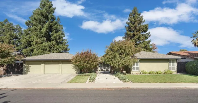 a view of yellow house with a yard and large trees