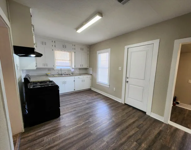 a kitchen with granite countertop a refrigerator a stove a microwave and white cabinets with wooden floor