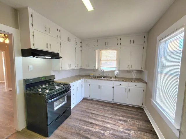 a kitchen with granite countertop white cabinets appliances and a window