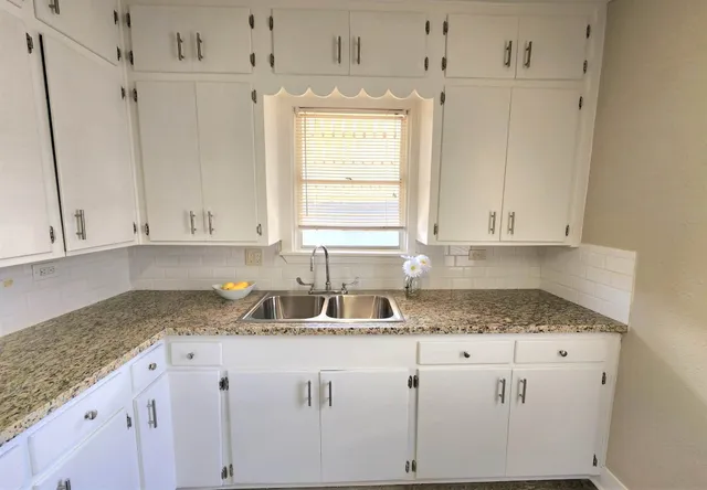 a kitchen with granite countertop white cabinets and a sink