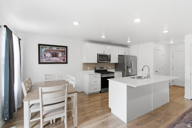3808 Galatia Road Magna, UT 84044 - Photo 13 of 59 Kitchen and dining area featuring white cabinetry, stainless steel appliances, a center island with sink, recessed lighting, and wood-finish flooring