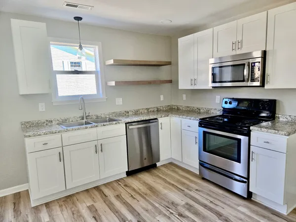 a kitchen with granite countertop white cabinets stainless steel appliances a sink and a window