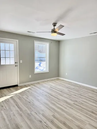 an empty room with wooden floor chandelier fan and windows