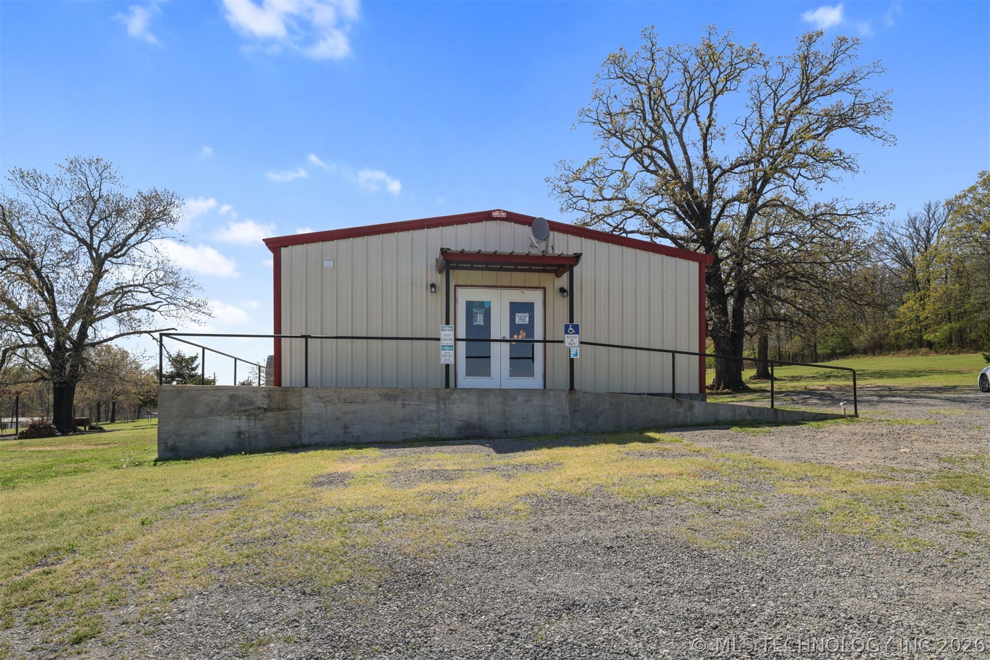 3565 Sawmill Road Caddo, OK 74729 - Photo 3 of 32 Metal siding structure with a red trim roof, double entry doors, a concrete ramp, and a black metal handrail