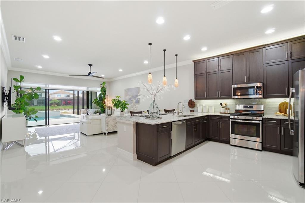 4318 Aurora Street Naples, FL 34119 - Photo 11 of 50 Kitchen with stainless steel appliances, dark brown cabinets, a peninsula, light stone counters, and ornamental molding