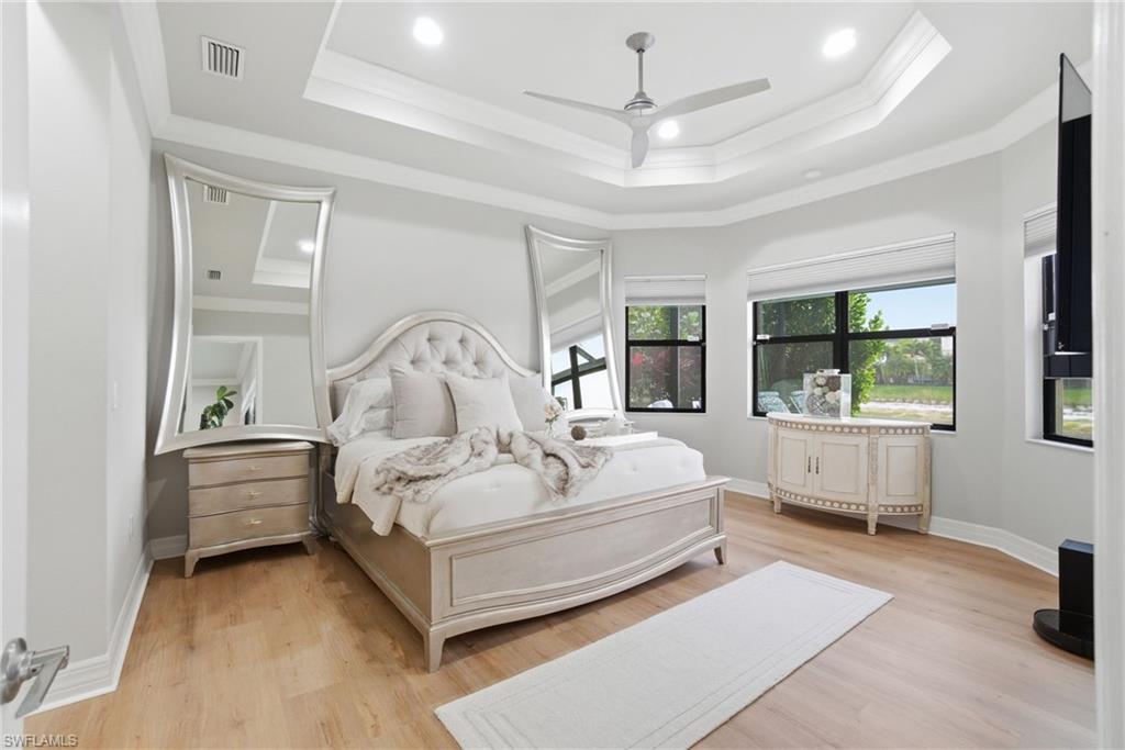 4318 Aurora Street Naples, FL 34119 - Photo 22 of 50 Light-filled primary bedroom featuring wood-style flooring, tray ceiling with crown molding, recessed lighting, and a ceiling fan. Large windows provide abundant natural light and serene views.
