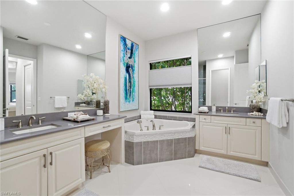 4318 Aurora Street Naples, FL 34119 - Photo 25 of 50 Light-filled primary bath with dual vanities, a relaxing soaking tub, recessed lighting, and expansive mirrors for a spa-like atmosphere.