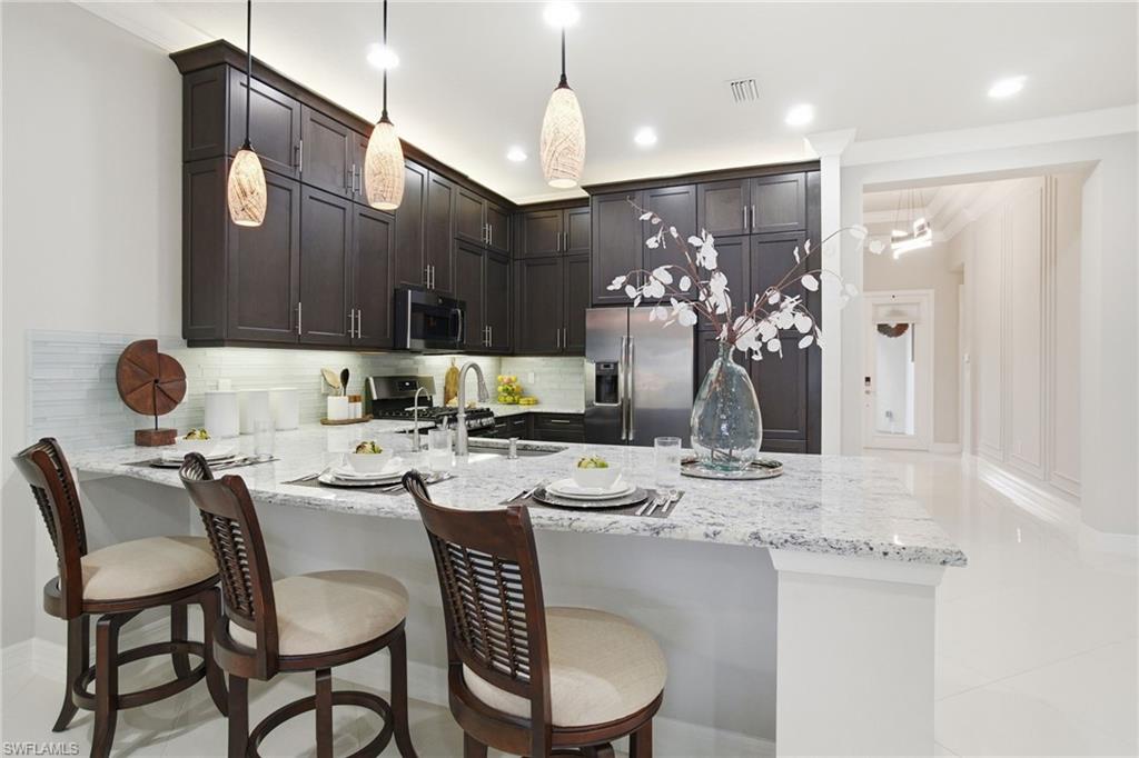 4318 Aurora Street Naples, FL 34119 - Photo 10 of 50 Kitchen featuring a peninsula, backsplash, light stone countertops, stainless steel appliances, and crown molding