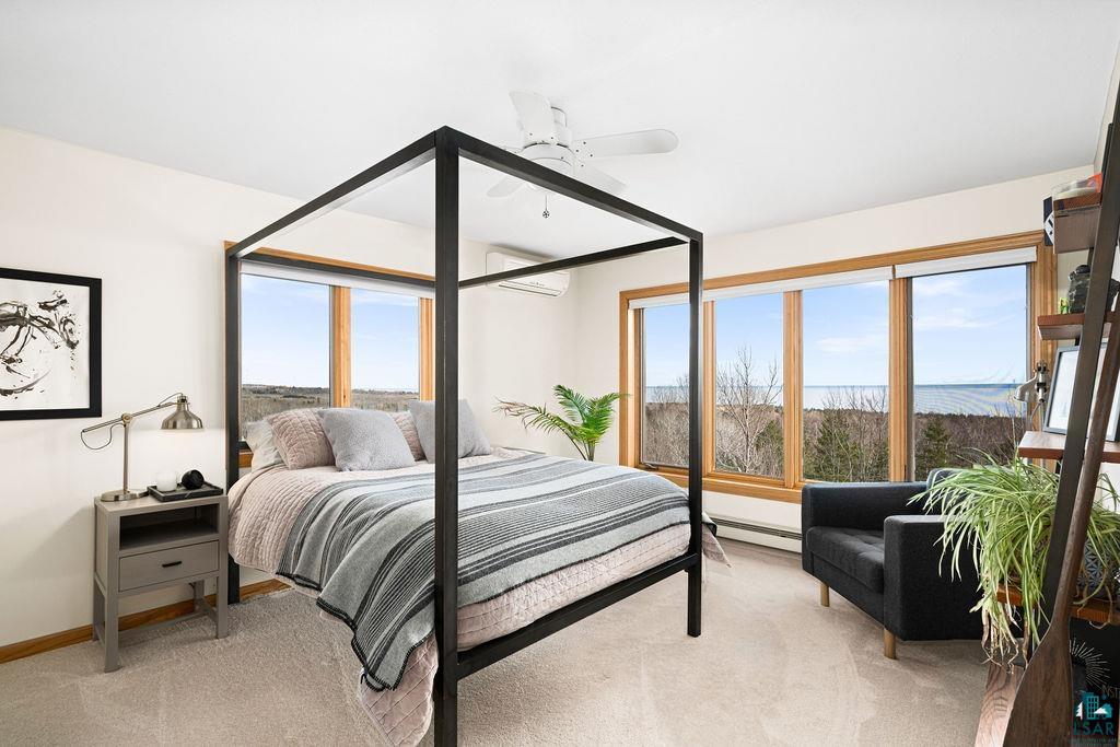4856 Kingston Street Duluth, MN 55804 - Photo 23 of 88 Light-filled bedroom featuring large picture windows with natural wood trim, soft carpeting, a ceiling fan, and an integrated wall-mounted heating/cooling unit