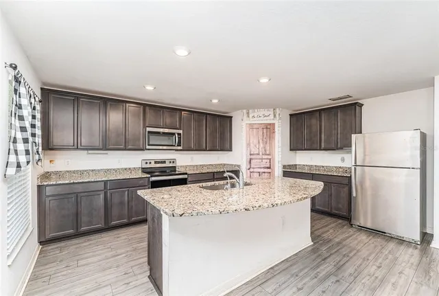 a kitchen with stainless steel appliances granite countertop a refrigerator a stove top oven a sink and dishwasher with wooden floor