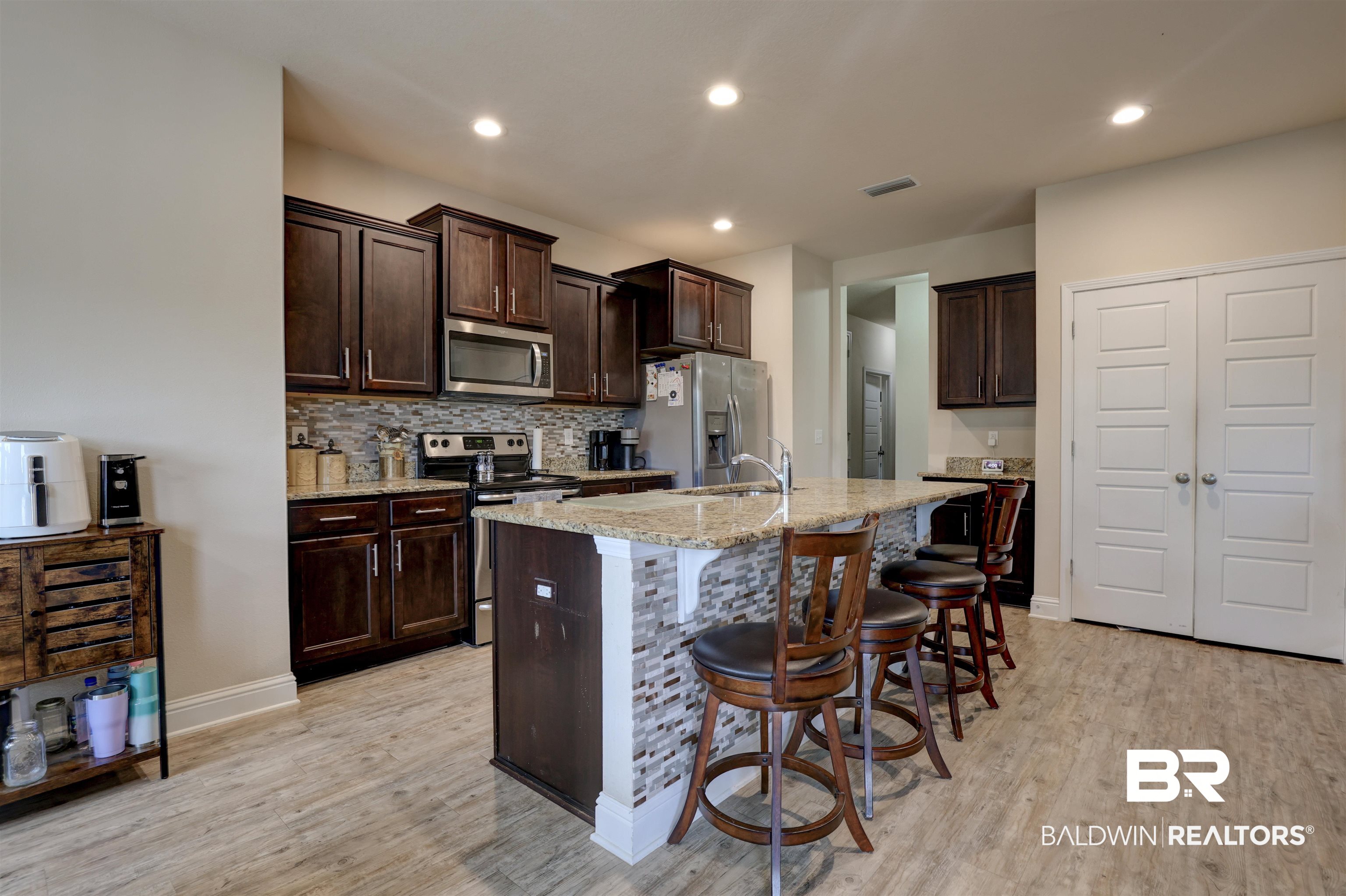 21902 Yosemite Boulevard Fairhope, AL 36532 - Photo 9 of 32 Kitchen featuring dark brown cabinetry, a center island with sink, stainless steel appliances, and light hardwood / wood-style floors