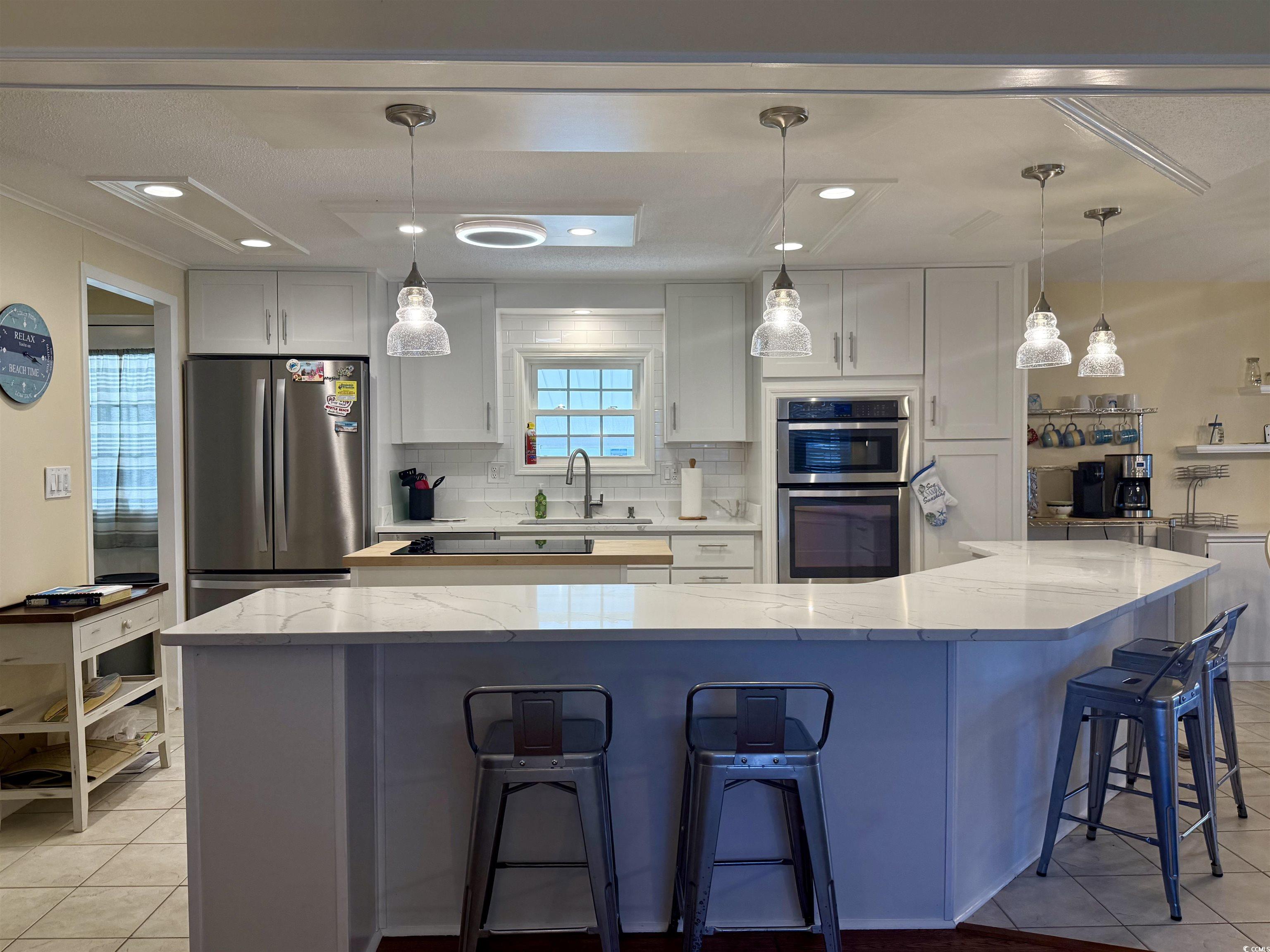 416 Oceanside Drive Surfside Beach, SC 29575 - Photo 17 of 37 Kitchen featuring appliances with stainless steel finishes, light tile patterned flooring, tasteful backsplash, white cabinetry, and light stone counters