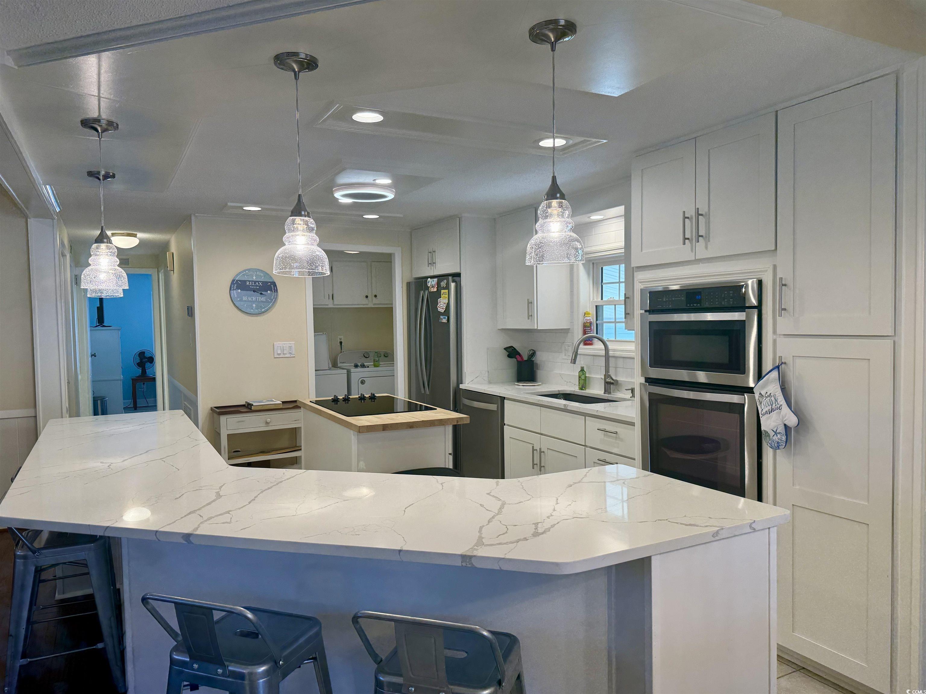 416 Oceanside Drive Surfside Beach, SC 29575 - Photo 4 of 37 Kitchen featuring stainless steel appliances, a kitchen island, separate washer and dryer, light stone countertops, and white cabinets