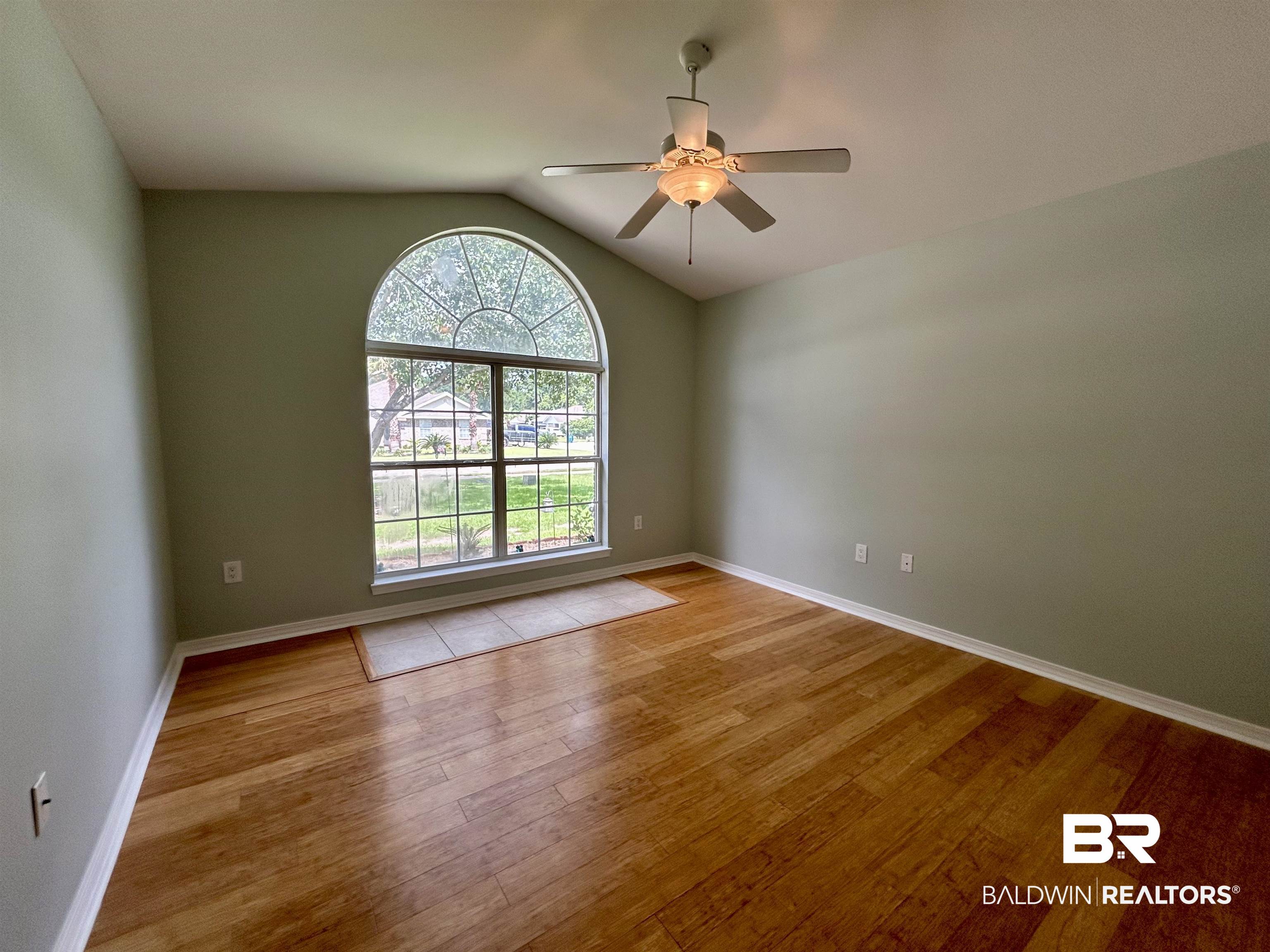 7198 Raintree Lane Gulf Shores, AL 36542 - Photo 19 of 33 Arch-top window with grid pattern, vaulted ceiling, wood-finish flooring, ceiling fan with light fixture, and neutral wall tones