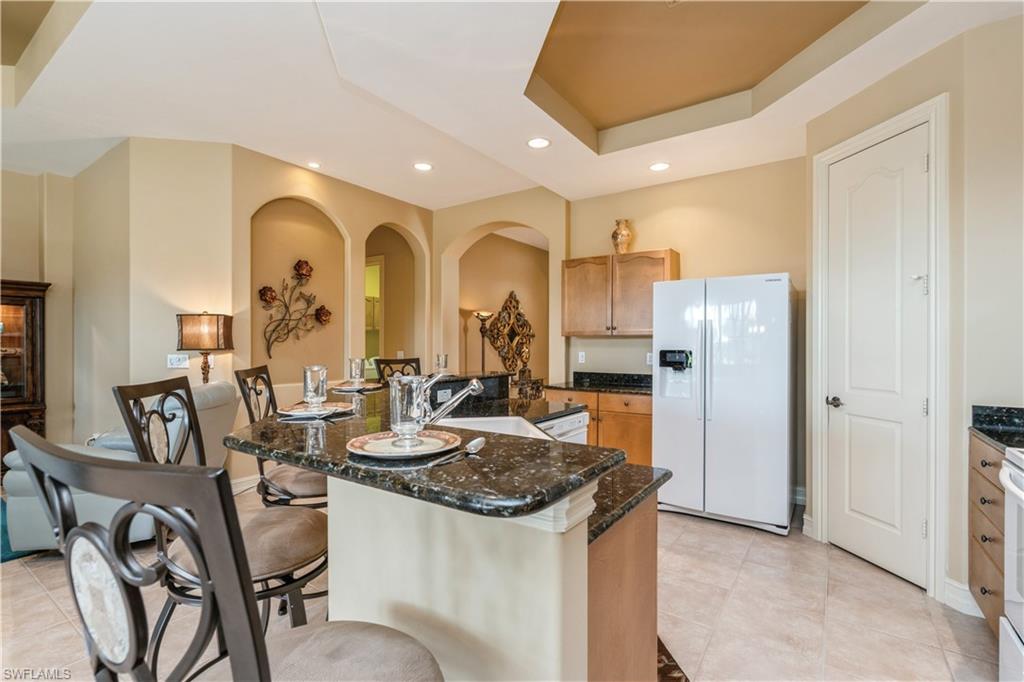 1411 Serrano Circle Naples, FL 34105 - Photo 17 of 50 Kitchen with a tray ceiling, sink, a center island with sink, dark stone countertops, and white fridge with ice dispenser