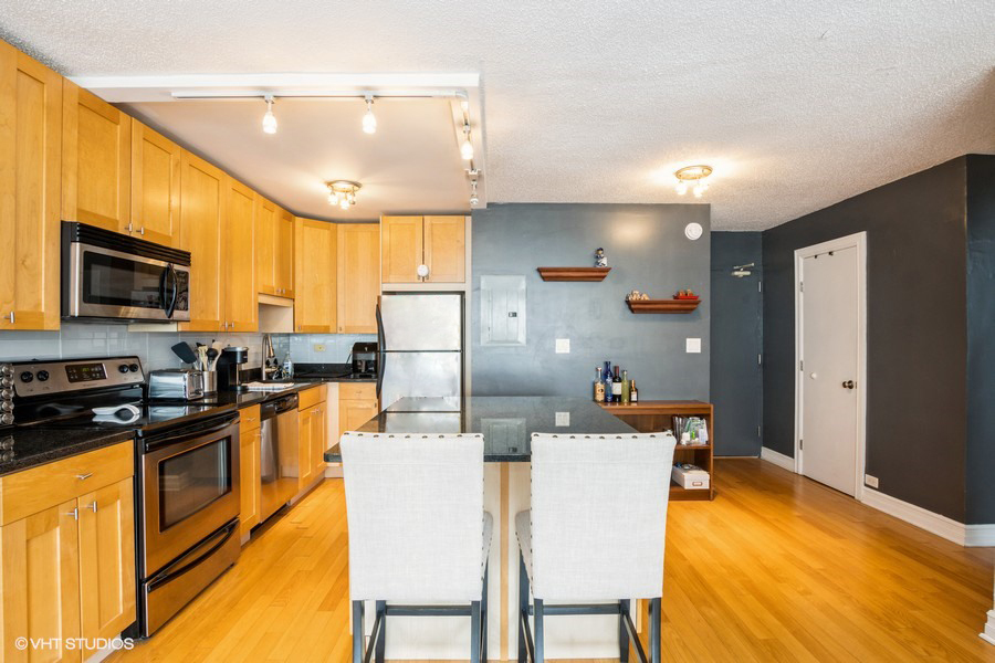 2930 North Sheridan Road, Unit 1008 Chicago, IL 60657 - Photo 4 of 12 a kitchen with stainless steel appliances a stove a refrigerator a sink dishwasher with a dining table and chairs
