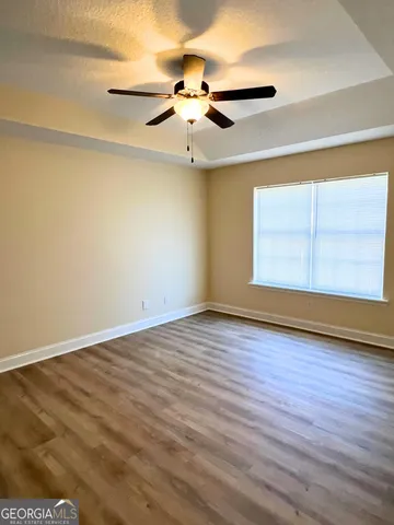 an empty room with wooden floor chandelier fan and windows