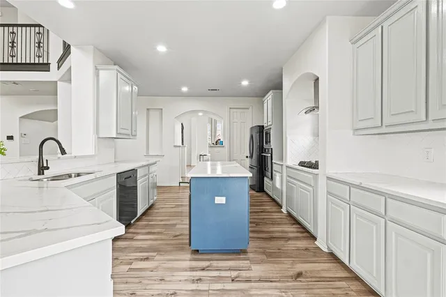a large kitchen with kitchen island a sink wooden floor and stainless steel appliances