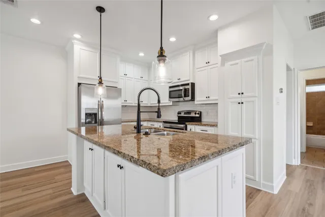 a kitchen with kitchen island granite countertop a sink a counter space appliances and cabinets