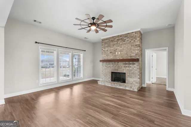 a view of an empty room with wooden floor fireplace and a window