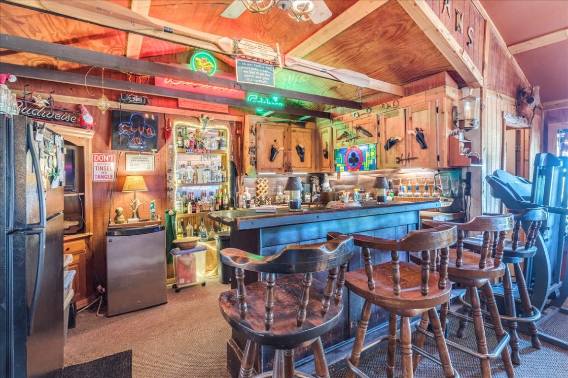 2411 Rohde Road Kyle, TX 78640 - Photo 18 of 40 Indoor dry bar featuring dark countertops, freestanding refrigerator, light colored carpet, stainless steel refrigerator, and brown cabinets