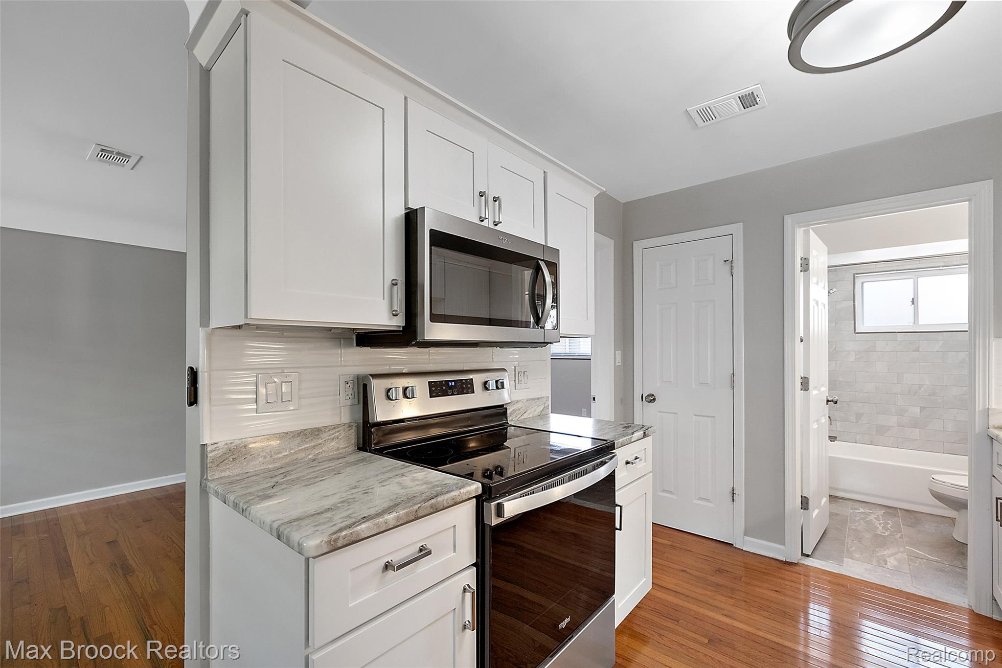 3905 Devon Road, Unit #4 Royal Oak, MI 48073 - Photo 10 of 21 White shaker cabinetry, stainless steel appliances, light-toned stone countertops, subway tile backsplash, and wood-finish flooring