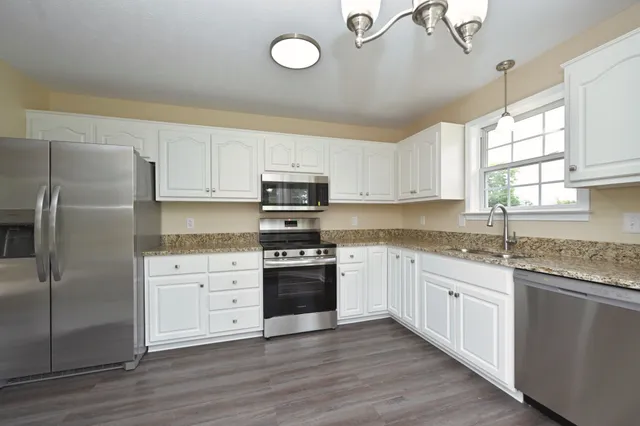 a kitchen with stainless steel appliances granite countertop a stove a sink dishwasher a refrigerator and white cabinets with wooden floor