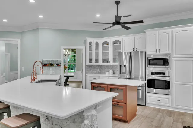 a kitchen with stainless steel appliances a sink a stove a refrigerator cabinets and chairs