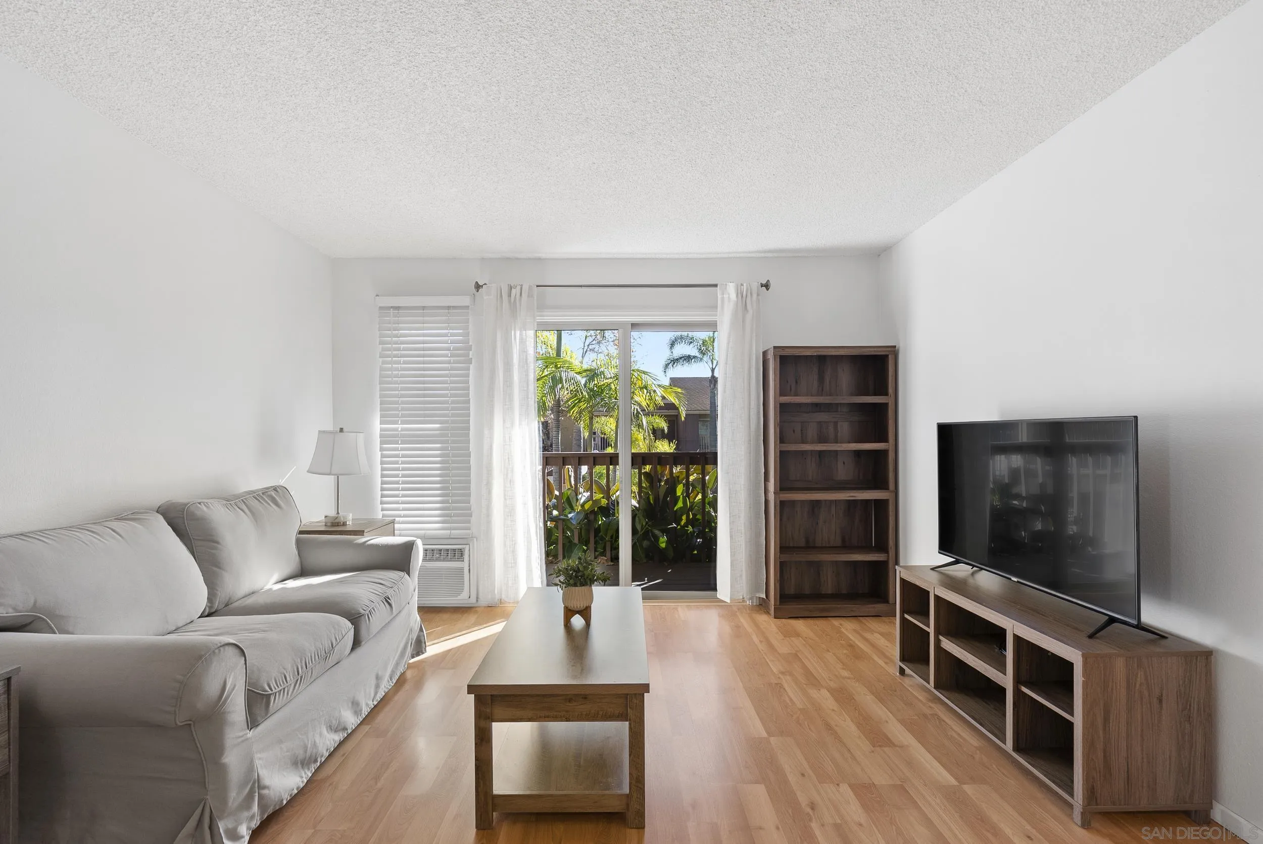 5978 Rancho Mission Road, Unit 274 San Diego, CA 92108 - Photo 5 of 23 a living room with furniture a flat screen tv and a floor to ceiling window