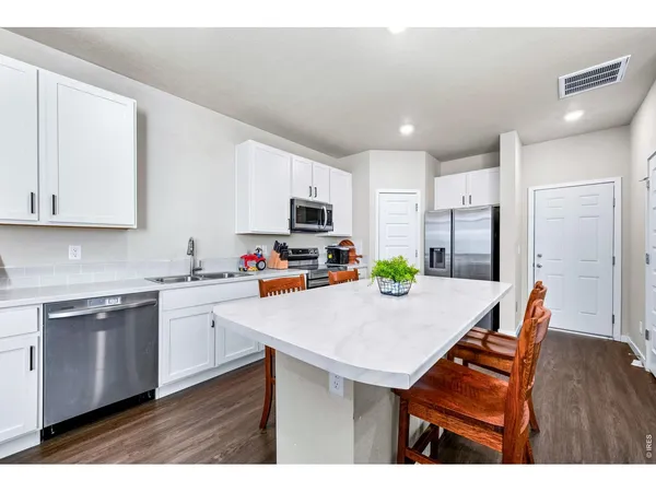 a kitchen with stainless steel appliances kitchen island granite countertop a refrigerator a stove top oven a sink dishwasher and white cabinets with wooden floor