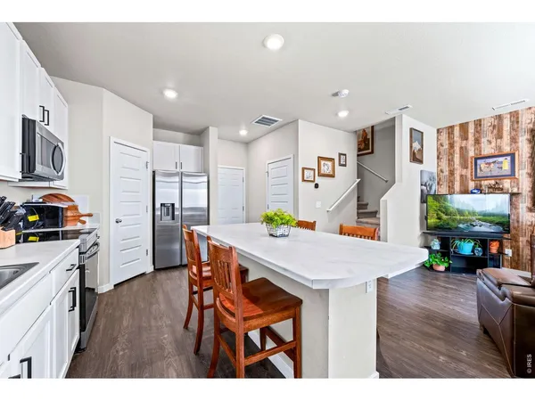 a open kitchen with stainless steel appliances kitchen island granite countertop a refrigerator a stove a sink dishwasher and white cabinets with wooden floor