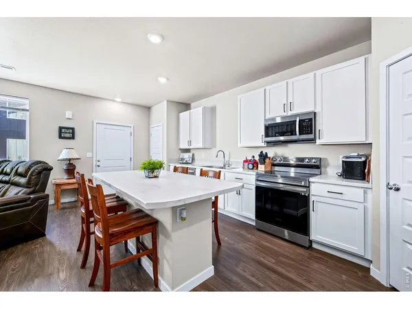 a open kitchen with stainless steel appliances a stove a sink a microwave a refrigerator white cabinets and wooden floor