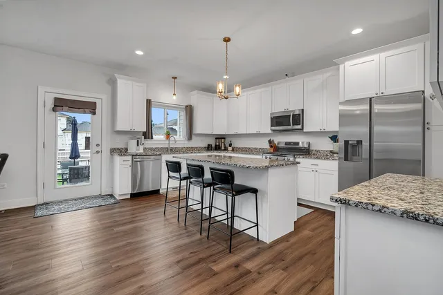 a kitchen with stainless steel appliances kitchen island granite countertop a refrigerator a stove a sink and white cabinets with wooden floor