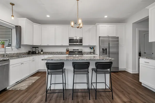 a kitchen with a refrigerator a stove top oven a sink dishwasher a dining table and chairs with wooden floor