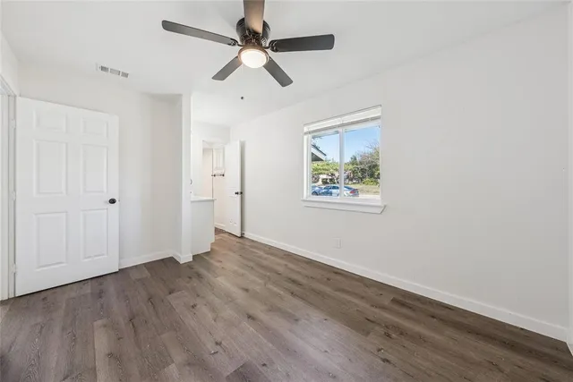 an empty room with wooden floor ceiling fan and windows