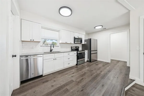 a kitchen with stainless steel appliances granite countertop a stove a sink dishwasher and a refrigerator with wooden floor