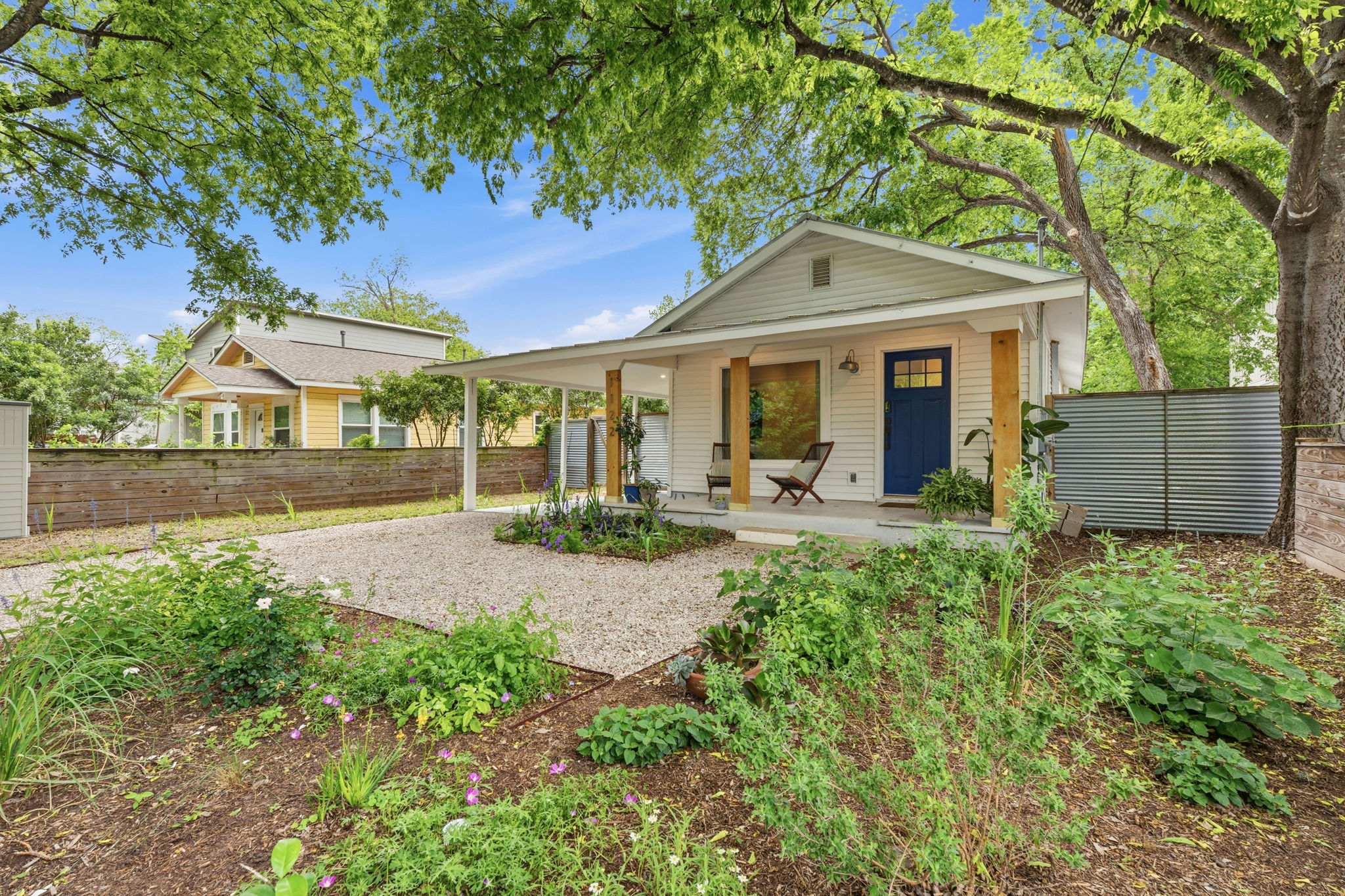 1122 Gunter Street Austin, TX 78702 - Photo 1 of 23 The property features a charming front porch with natural wood pillars and a vibrant blue entry door, set amidst lush green landscaping