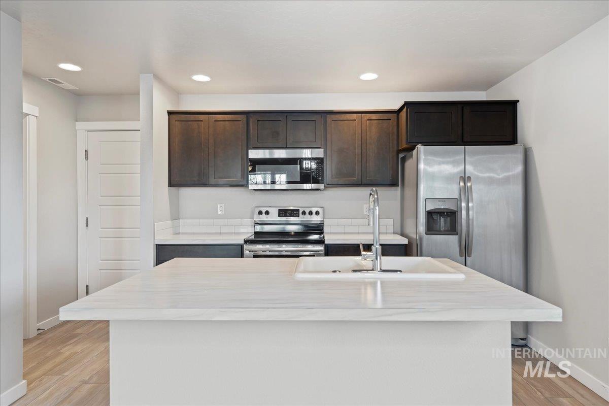 2471 East Goldstone Street Meridian, ID 83642 - Photo 11 of 27 Kitchen featuring appliances with stainless steel finishes, dark brown cabinets, recessed lighting, a center island with sink, and light wood-type flooring