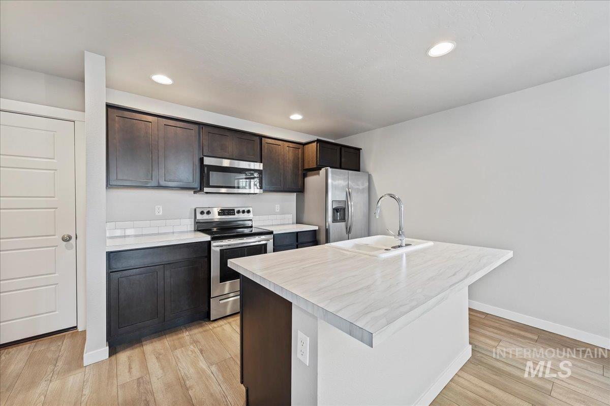 2471 East Goldstone Street Meridian, ID 83642 - Photo 9 of 27 Kitchen with appliances with stainless steel finishes, light countertops, dark brown cabinets, a kitchen island with sink, and recessed lighting