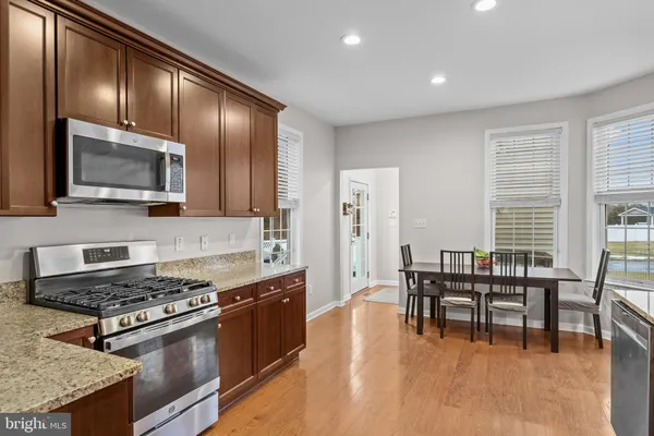 a kitchen with stainless steel appliances granite countertop a stove top oven a sink dishwasher a dining table and chairs with wooden floor