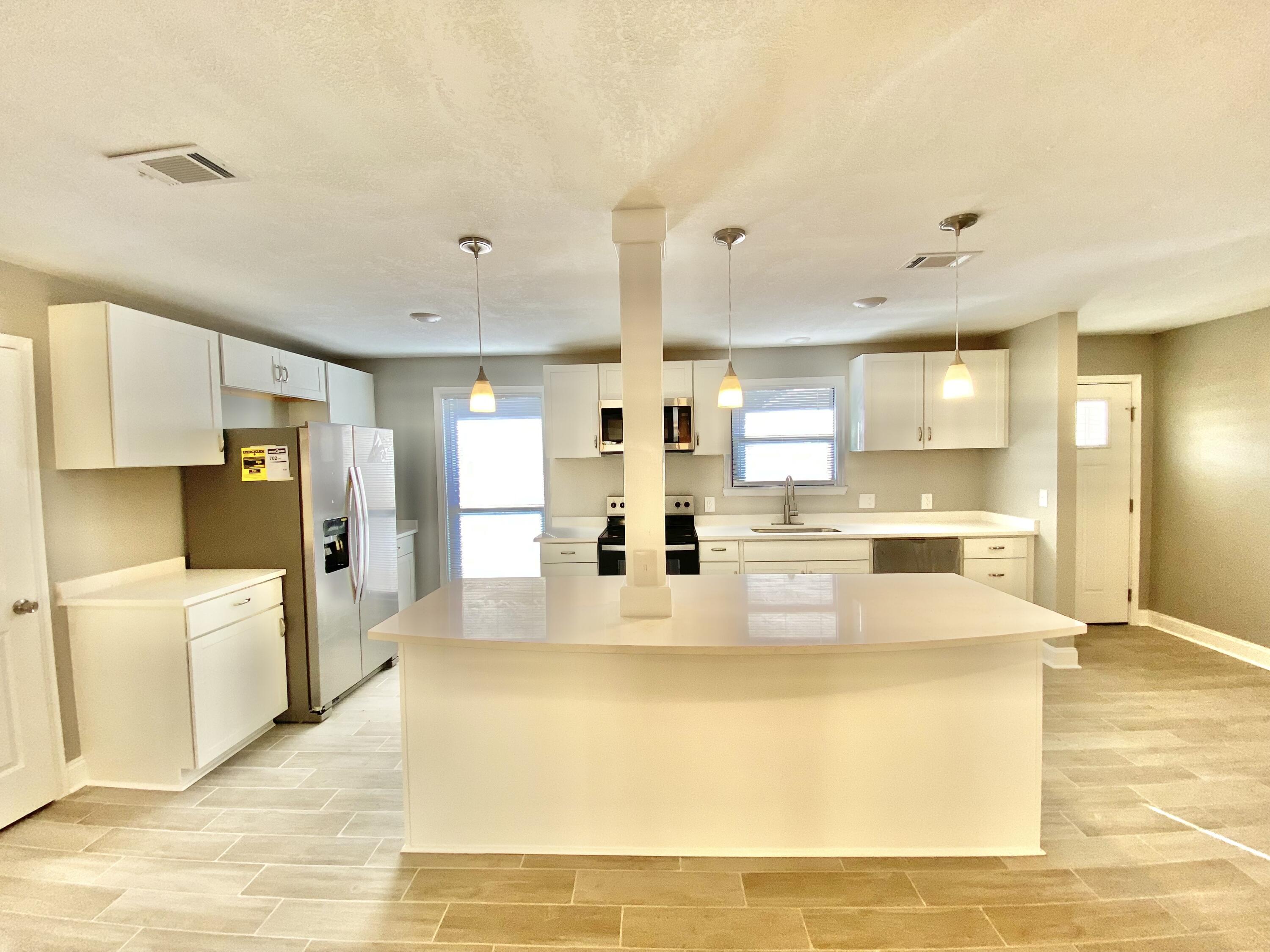 795 Bay Street Crestview, FL 32536 - Photo 11 of 34 a large white kitchen with kitchen island a stove a refrigerator cabinets and living room view