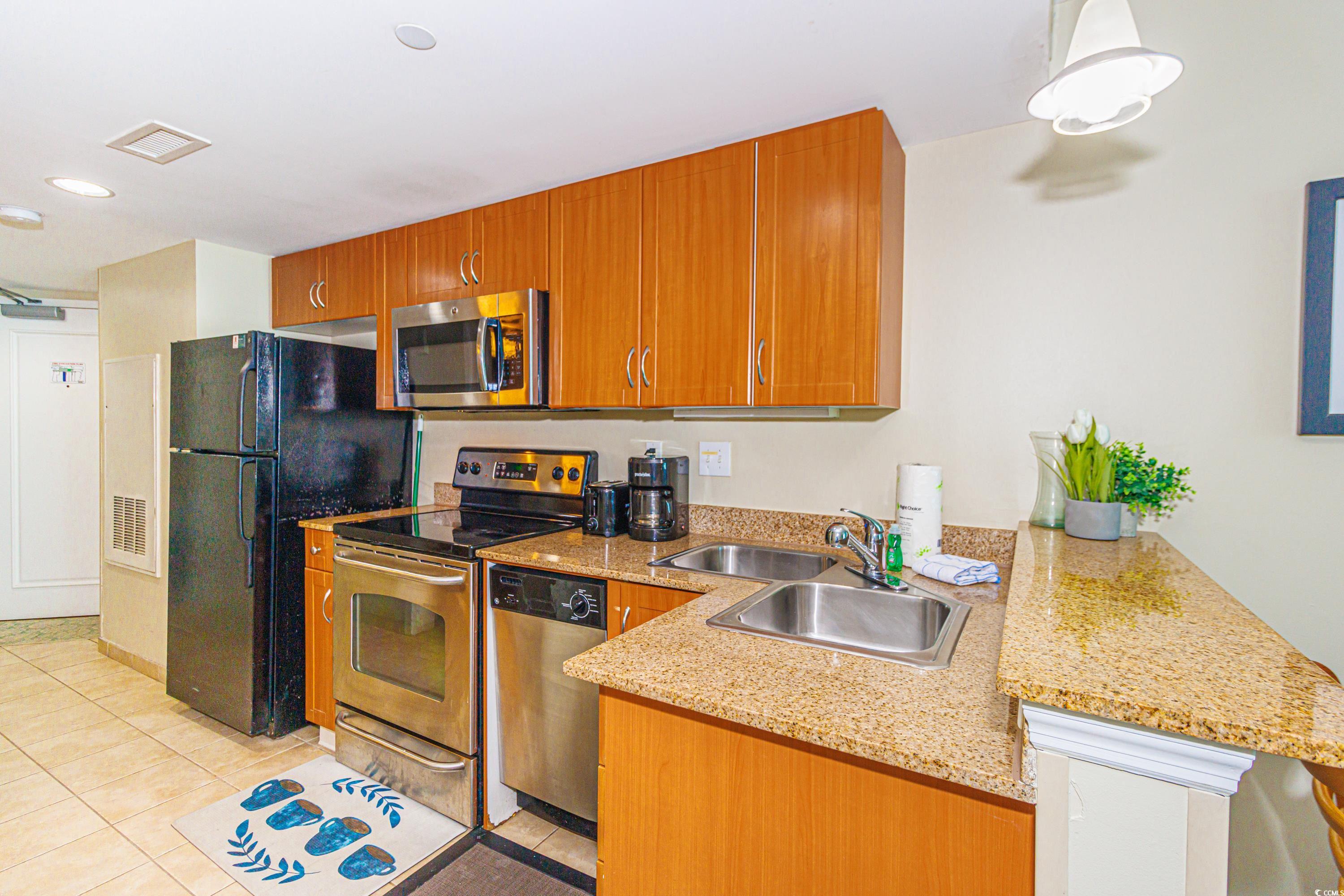 201 South Ocean Boulevard, Unit 1610 Myrtle Beach, SC 29577 - Photo 14 of 40 Kitchen with stainless steel appliances, light stone counters, light tile patterned floors, brown cabinets, and a peninsula
