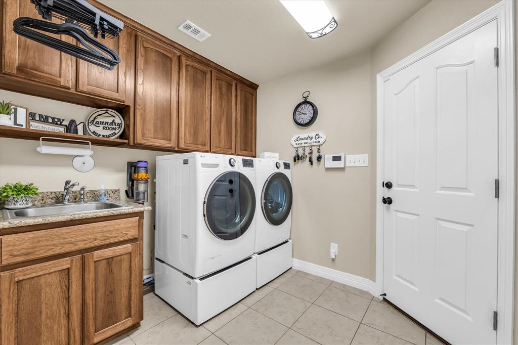 910 Springdale Lane Lorena, TX 76655 - Photo 27 of 39 Utility room featuring a built-in sink, wood-finish cabinetry, light-toned tile flooring, and a white paneled door