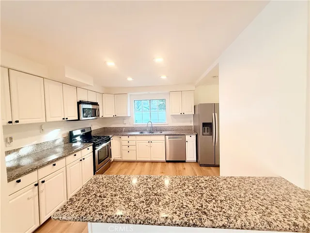 a large white kitchen with stainless steel appliances granite countertop a stove top oven a sink and white cabinets