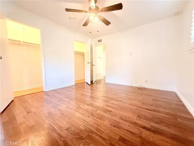 a view of an empty room with wooden floor and a ceiling fan