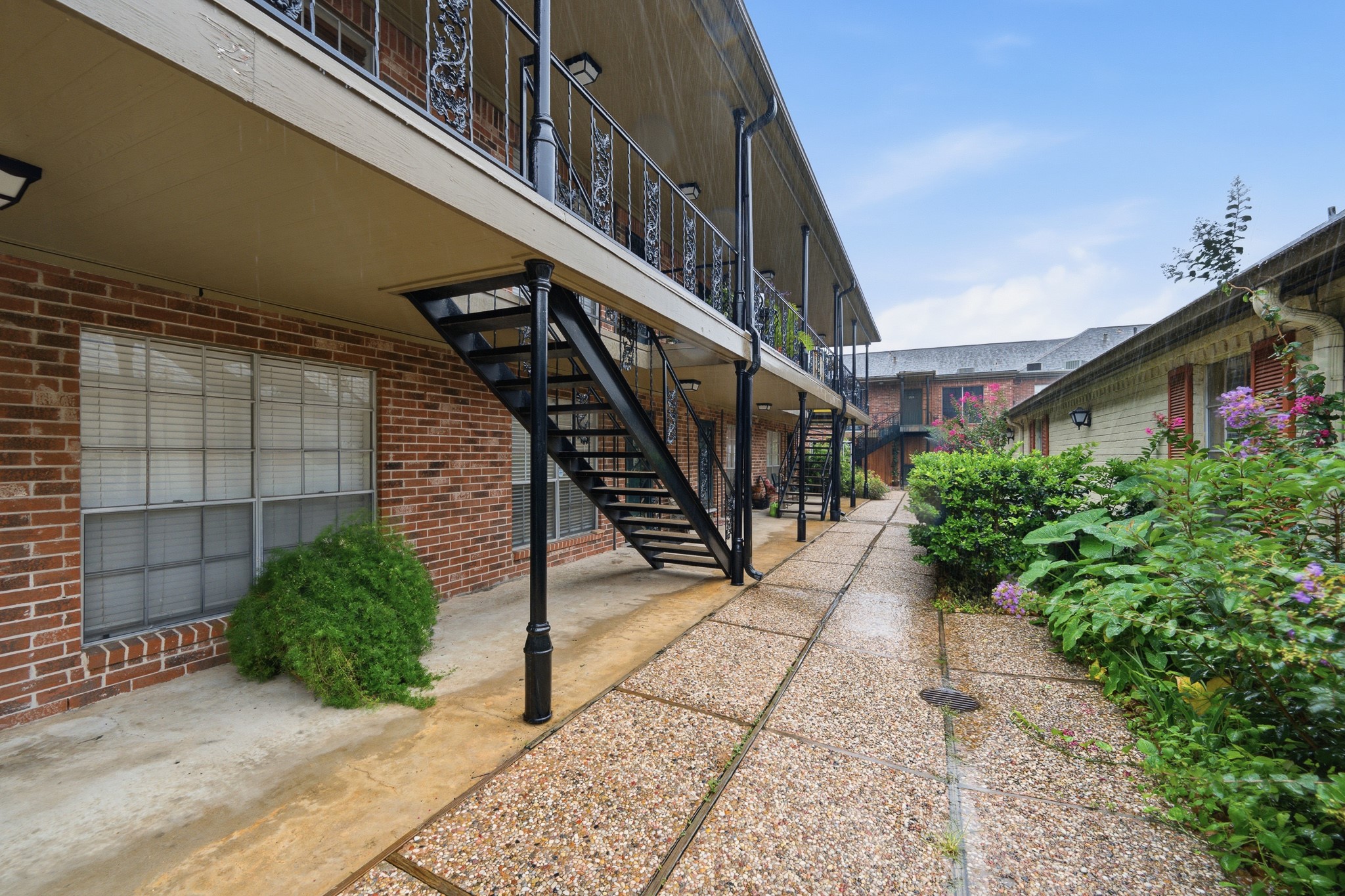 11550 Chimney Rock Road, Unit 133 Houston, TX 77035 - Photo 25 of 40 Charming brick condominium complex with a well-maintained walkway, featuring lush greenery and decorative wrought iron railings.
