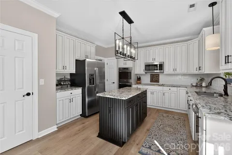a kitchen with stainless steel appliances granite countertop a refrigerator a stove a sink dishwasher a oven with white cabinets and wooden floor