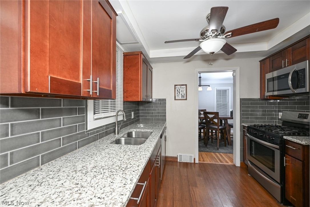 3699 Bainbridge Road Cleveland Heights, OH 44118 - Photo 16 of 37 Kitchen featuring wood-finish cabinetry, granite-style countertops, stainless steel appliances, a double basin sink with a gooseneck faucet, and subway tile backsplash