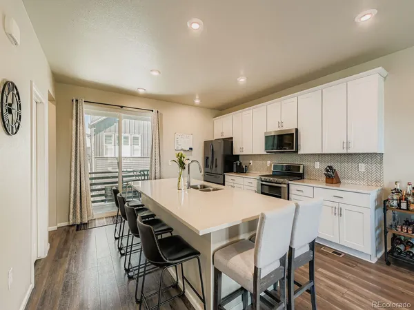 a kitchen with stainless steel appliances a stove top oven a refrigerator a sink and a dining table with wooden floor