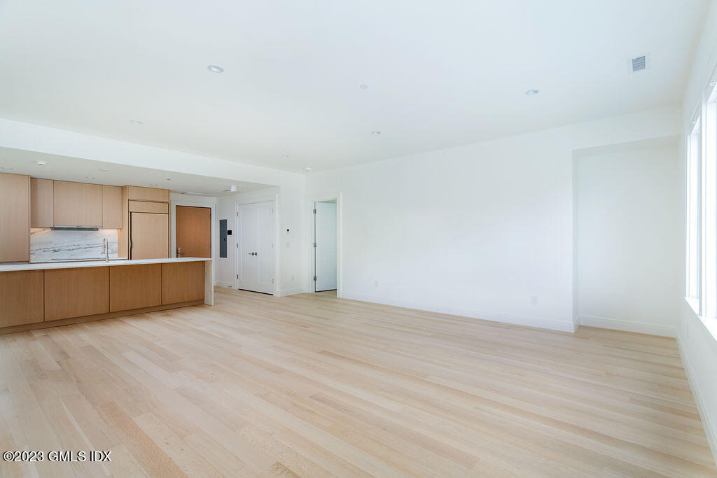 89 River Road, Unit 203 Cos Cob, CT 06807 - Photo 11 of 27 a view of an empty room with wooden floor and a kitchen